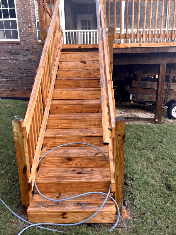 Wooden staircase leading to a deck, showcasing polished steps and surrounding grass.