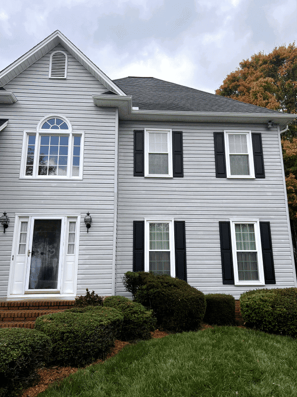 Gray two-story house with black shutters, white trim, and well-maintained shrubs.