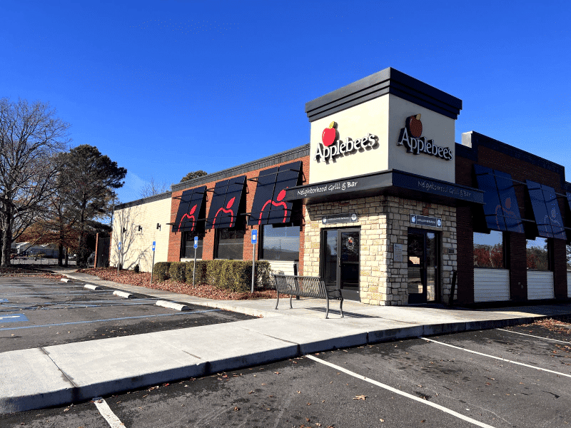 Applebee's restaurant exterior with outdoor seating and clear blue sky background.