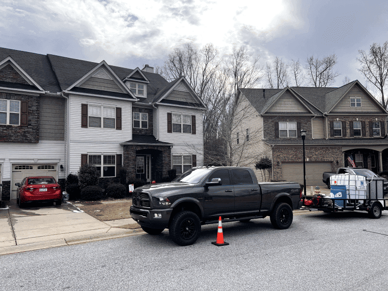 Dark truck parked on a residential street near two houses and a trailer with equipment.