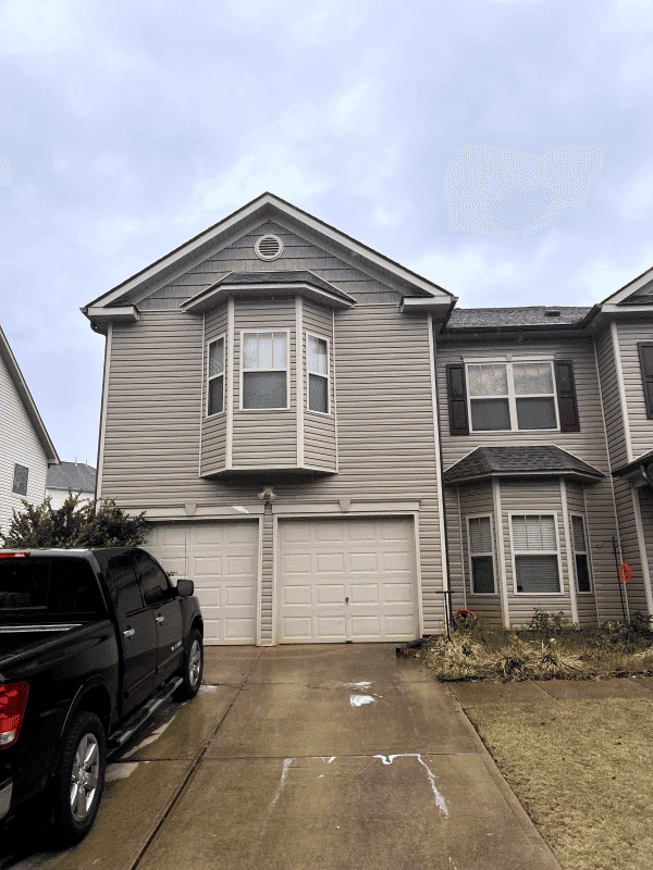 Two-story beige house with bay window, double garage, and driveway in overcast weather.