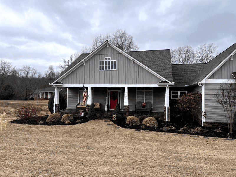 Charming gray house with red door and landscaped yard under cloudy sky. Ideal suburban home.