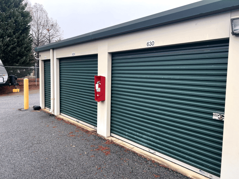 Storage unit facility with green roll-up doors and a fire extinguisher mounted on the wall.
