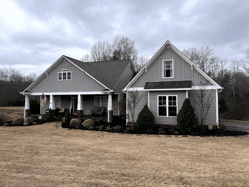 Modern gray house with a front porch, flag, and landscaped yard under a cloudy sky.