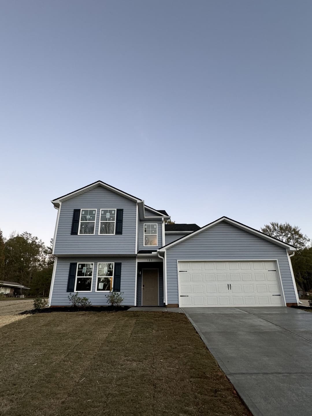 Two-story blue house with white trim, garage, and landscaped front yard at dusk.