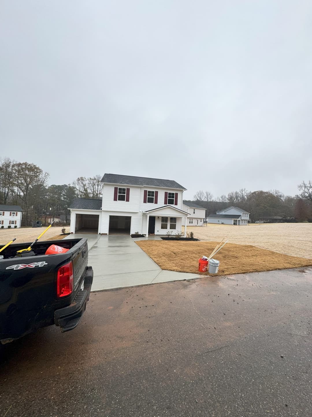 Two-story house with a driveway on a rainy day, surrounded by grassy lawns.