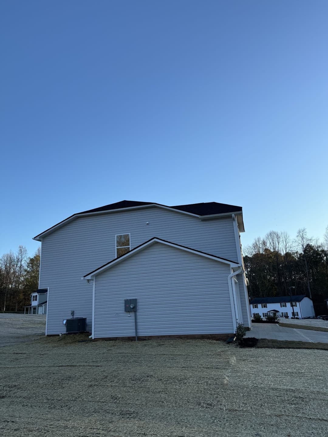 Modern two-story house with a clear blue sky, featuring a side view and adjacent buildings.