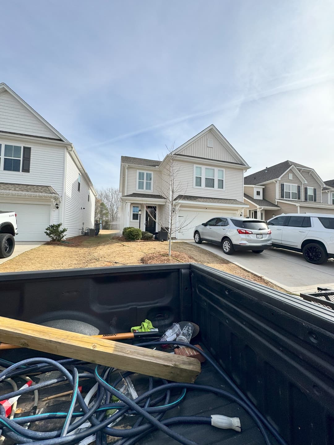 View of a suburban home with parked cars, from a pickup truck's bed filled with tools.