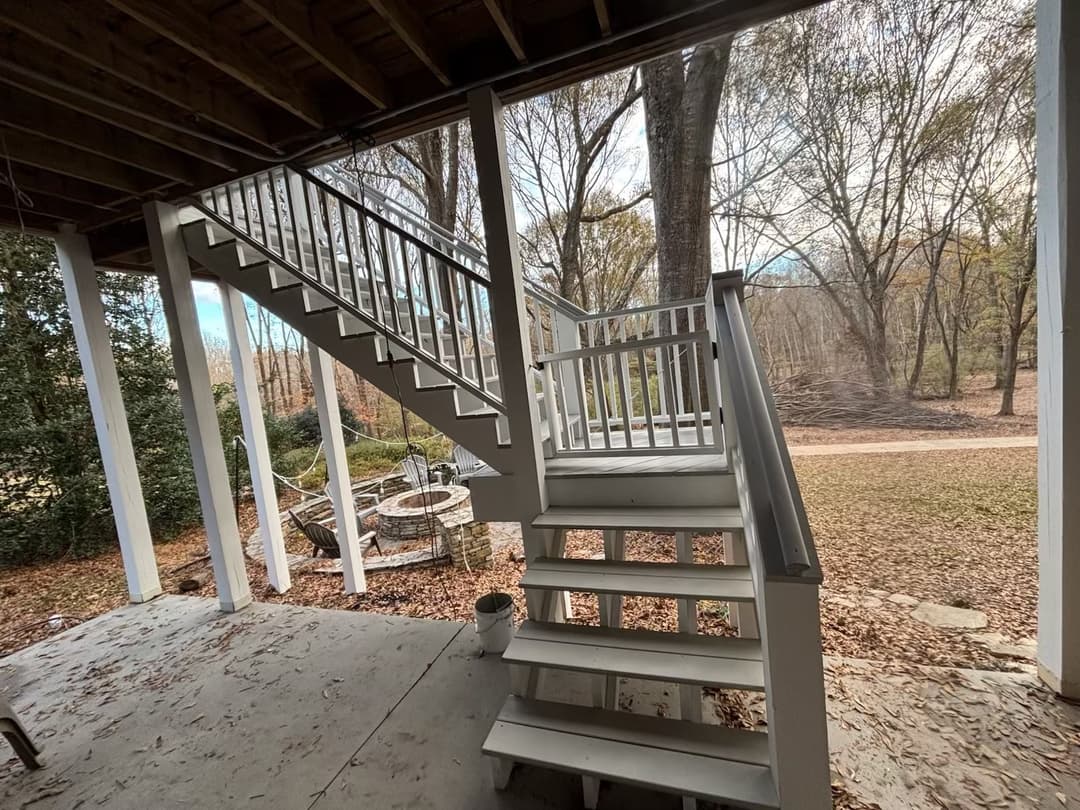 Outdoor staircase leading to a raised porch in a wooded setting with leaf-covered ground.