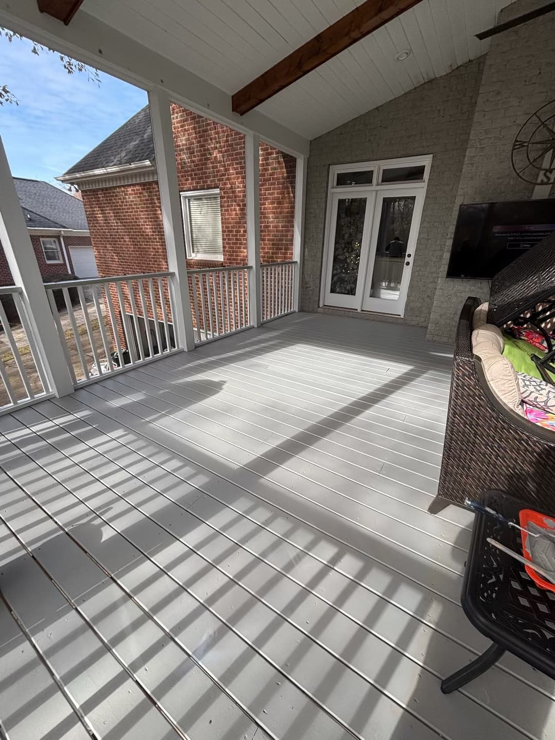 Spacious screened porch with gray flooring, and a wicker sofa, bright natural light.