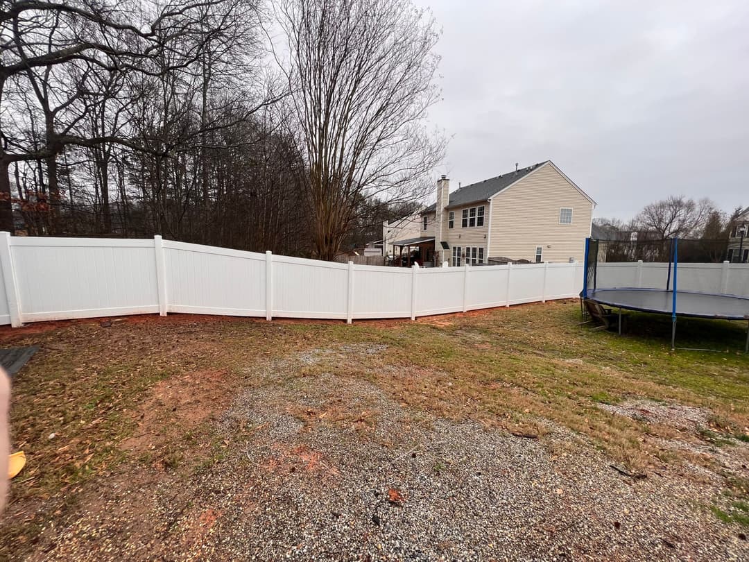 White vinyl fence surrounding backyard with trampoline and house in the background.