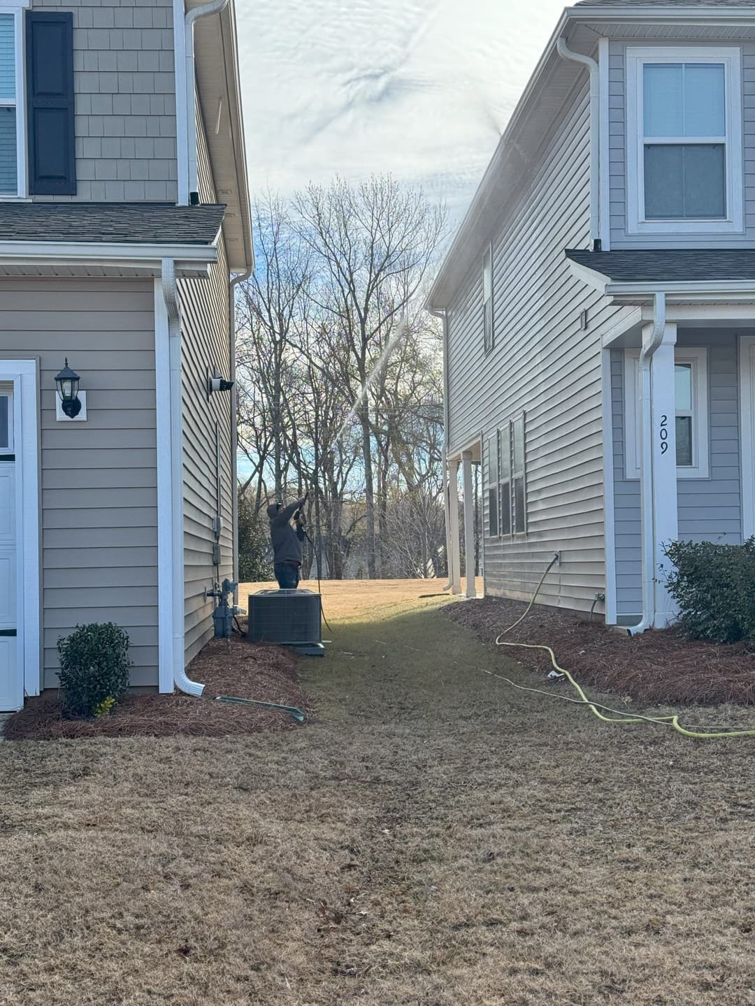 Person watering the lawn between two residential houses on a sunny day.