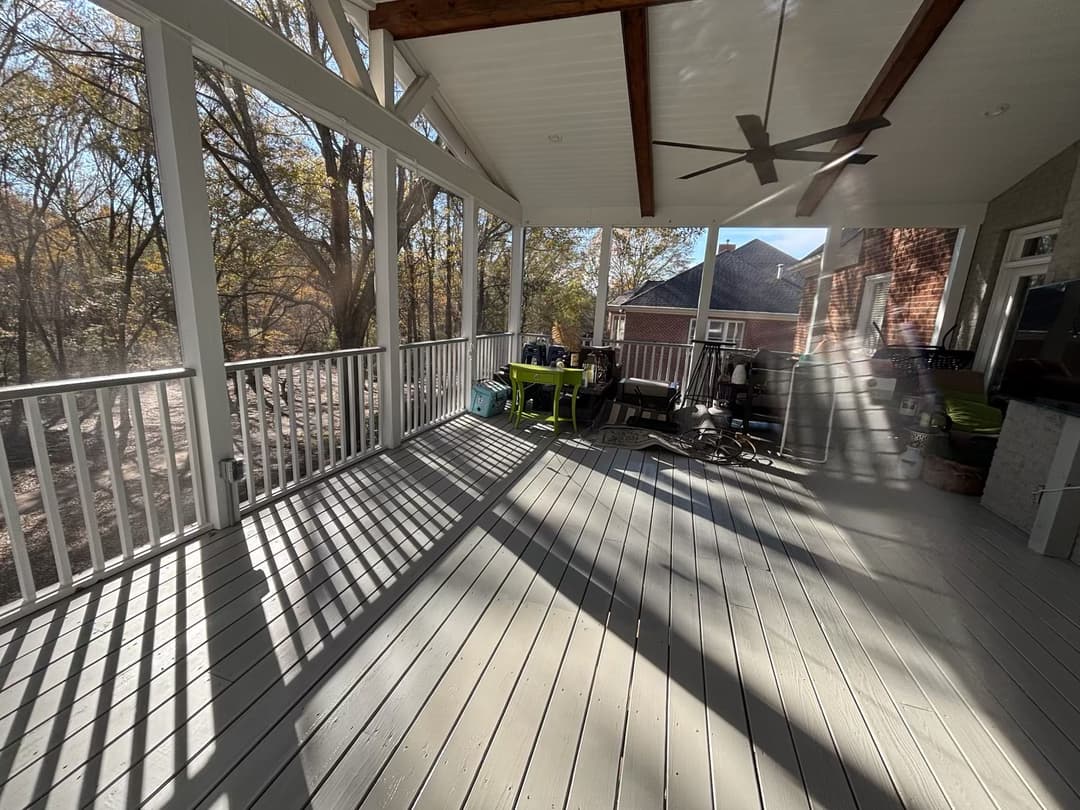 Spacious screened porch with wooden beams, outdoor furniture, and sunlight casting shadows.