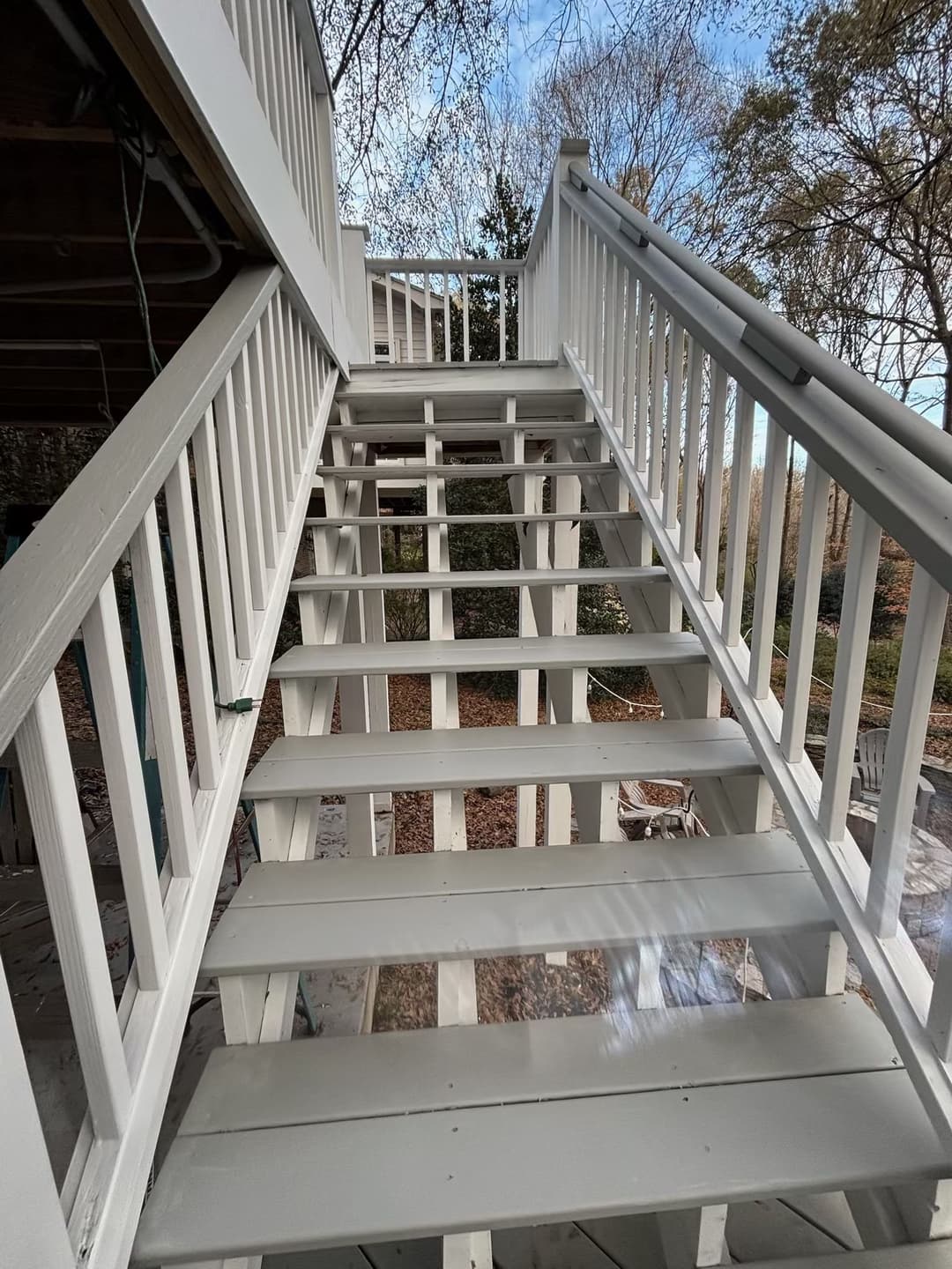White outdoor stairs leading up to a deck surrounded by trees and a clear blue sky.