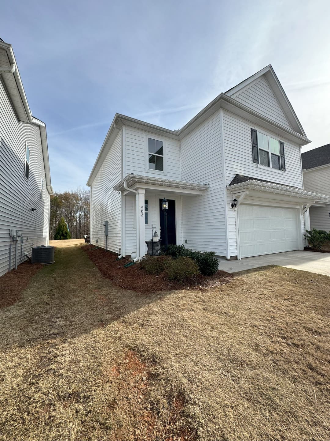 Two-story white house with a garage and landscaped front yard in a suburban neighborhood.